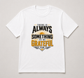 A white short-sleeve crewneck t-shirt with a graphic print on the front that reads 'THERE IS ALWAYS SOMETHING TO BE GRATEFUL FOR' in black and gold lettering with a sunburst design, displayed flat against a light gray background.