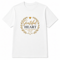 A white short-sleeve crewneck t-shirt with a gold and black graphic on the chest featuring a wreath, a heart, and the words 'Grateful HEART' and 'COUNT YOUR BLESSINGS EVERY DAY'.