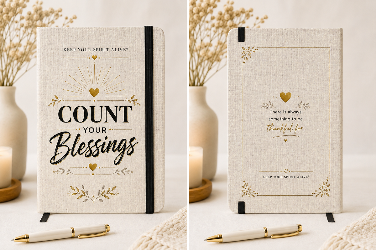 Two cream-colored hardcover notebooks with black and gold decorative text and floral accents, shown side by side on a light surface with dried flowers, candles, and a pen nearby.
