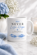 White gloss ceramic mug featuring the Never Lose Hope design with a blue watercolour mountain landscape and the quote "Hope is the light that guides you through the darkest days."