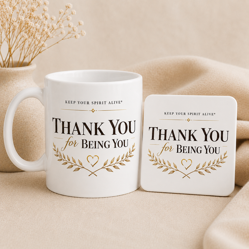 A white ceramic mug and matching square coaster set with the printed message 'THANK YOU for BEING YOU' in black and gold, styled on a beige fabric surface with dried flowers in the background.